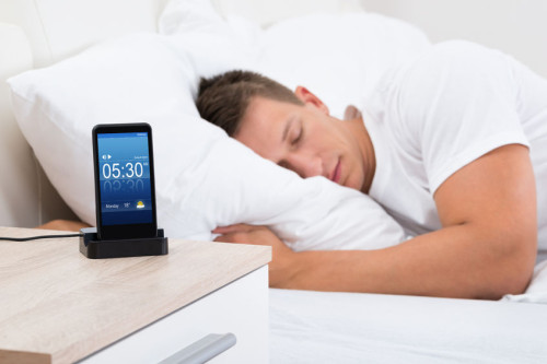 45165506 - young man sleeping on bed with alarm on mobile phone display