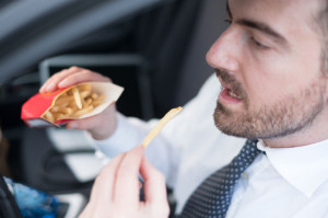 81052890 - man eating junk food and driving seated in his car