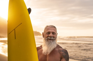 Happy fit senior having fun surfing at sunset time - Sporty bear